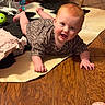 baby, child, red_hair, smiling, lying_down, cowhide_rug, wooden_floor, toy, stuffed_animal, indoor, clothing, person, happy, cute, playful, floor, hand, foot, home, infant