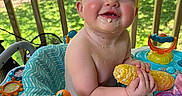Avery joined the competition — help win amazing prizes! baby, child, corn_on_the_cob, food, smile, rosy_cheeks, activity_center, toy, outdoor, porch, greenery, sunlight, happy, messy_face, seat, infant, cheerful, playtime, summer, cute