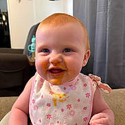 Avery is registered to the contest to win money with this photo: baby, child, infant, high_chair, bib, food_smear, smiling, red_hair, blue_eyes, indoor, home, furniture, curtains, deer_skull, wall_decor, cute, happy, portrait, person, sitting
