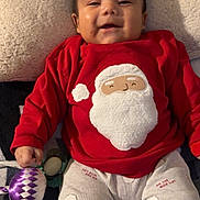 Derek Caleth is registered to the contest to win money with this photo: baby, child, smiling, red_clothing, santa_clothing, pajamas, toy, blanket, indoor, cute, holiday, christmas, face, person, happy, infant, lying_down, cozy, comfort, festive