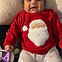 baby, child, smiling, red_clothing, santa_clothing, pajamas, toy, blanket, indoor, cute, holiday, christmas, face, person, happy, infant, lying_down, cozy, comfort, festive