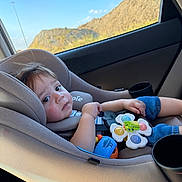 Khalid is registered to the contest to win money with this photo: baby, blue_sky, car, car_seat, child, colorful_toy, face, hills, infant, mountains, outdoor, portrait, road_trip, safe, sitting, sunny, toy, travel, vehicle, young_child