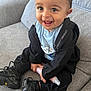 toddler, smiling, child, sitting, indoor, couch, clothing, jacket, sneakers, bottle, happy, person, face, black_clothing, footwear, baby, cute, young_child, home, casual