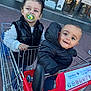 Khemys participe au concours pour gagner de l'argent avec cette photo : child, toddler, shopping_cart, pacifier, black_jacket, bow, outdoor, store_entrance, carrefour, happy, smiling, playful, clothing, pavement, metal, retail, urban, person, cute, fun
