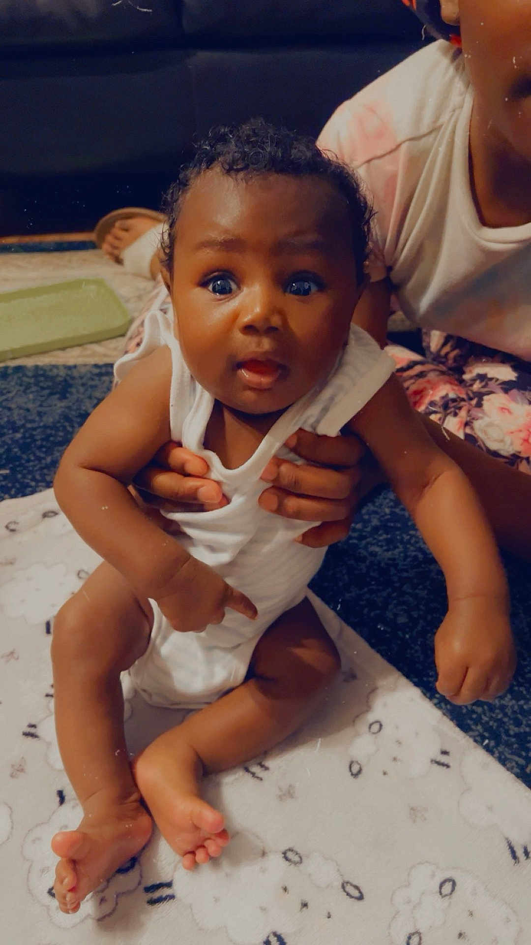 Khyzun Cooper is registered to the contest to win money with this photo: baby, child, infant, person, hands, blanket, curly_hair, indoor, carpet, white_clothing, cute, expression, skin, face, foot, toe, sitting, holding, pattern, floor