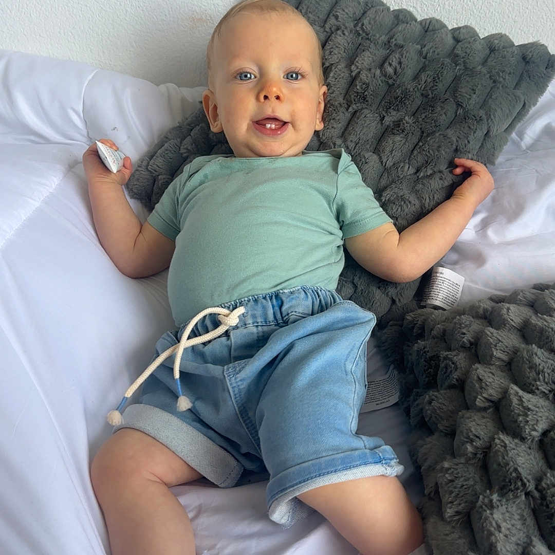Lizyo participe au concours pour gagner de l'argent avec cette photo : toddler, child, bed, pillow, white_bed_sheet, smiling, casual_clothing, denim_shorts, mint_green_shirt, socks, indoor, relaxed, holding_object, plush_pillow, happy, portrait, baby, cute, young_child, person