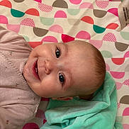 Amelia is registered to the contest to win money with this photo: baby, blanket, child, clothing, colorful, cute, eyes, face, happy, head, indoors, infant, lying_down, patterned_blanket, person, portrait, skin, smiling, soft_blanket, teeth