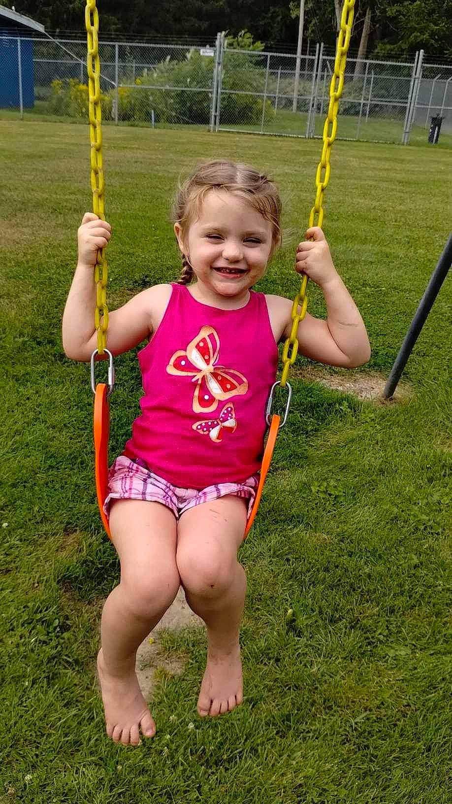 Anna is registered to the contest to win money with this photo: baby_toddler_clothing, city, fun, grass, happy, joy, leisure, outdoor_play_equipment, people, people_in_nature, person, plant, playground, recreation, shorts, smile, summer, swing, thumb, toddler