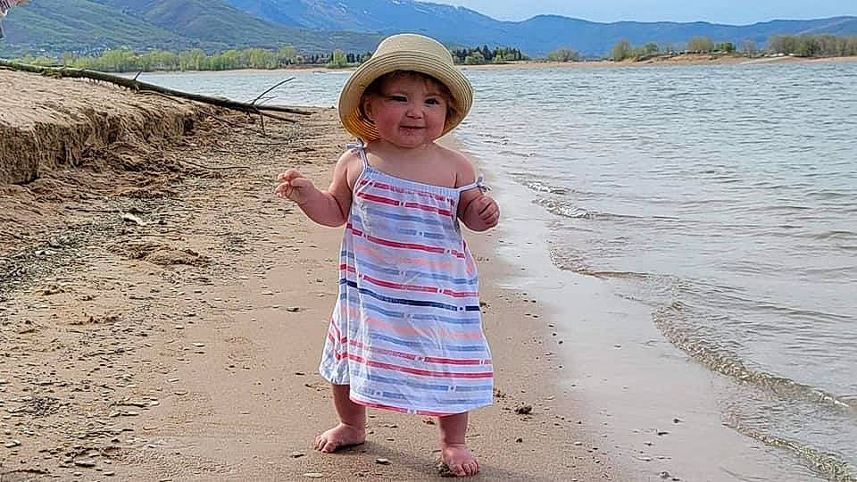 Lilith is registered to the contest to win money with this photo: beach, body_of_water, coastal_and_oceanic_landforms, happy, hat, headwear, joy, lake, landscape, natural_environment, people_in_nature, person, sand, shore, skin, sky, sleeve, summer, sun_hat, toddler