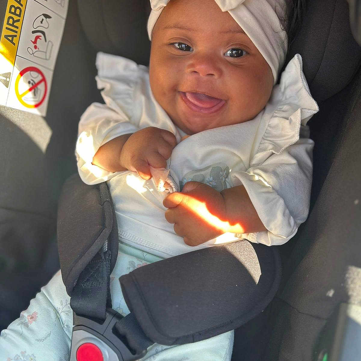 Azariah is registered to the contest to win money with this photo: baby, car_seat, child, close_up, clothing, cute, funny_face, happy, headband, indoors, infant, person, portrait, safety, seatbelt, smiling, sunlight, toddler, white_clothing, young_child