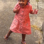 Tania is registered to the contest to win money with this photo: toddler, child, girl, smiling, playful, outdoor, sidewalk, concrete, grass, dress, coral, sandals, braids, purple_beads, happy, person, standing, cute, young, joyful