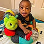 baby, child, smiling, indoor, plush_toy, caterpillar, colorful, sitting, red_socks, black_clothing, playful, happy, face, person, floor, door, carpet, toy, infant, cute