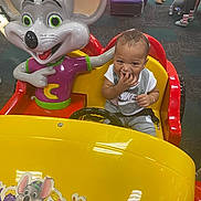 Lee joined the competition — help win amazing prizes! toddler, child, kiddie_ride, arcade, toy_car, mouse_figure, yellow, red, indoor, play, fun, giggle, clothing, person, smile, seatbelt, floor, background, people, entertainment