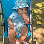 Lee is registered to the contest to win money with this photo: baby, child, stroller, outdoor, sun_hat, blue_clothing, shorts, barefoot, grass, sunlight, shadow, hand, face, person, summer, nature, leaves, infant, cute, relaxed