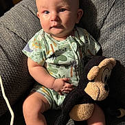 Wyatt joined the competition — help win amazing prizes! baby, child, stuffed_toy, monkey, onesie, dinosaur_pattern, chair, gray, soft_toy, plush, indoor, cute, infant, portrait, sitting, expression, light, warm, texture, comfort