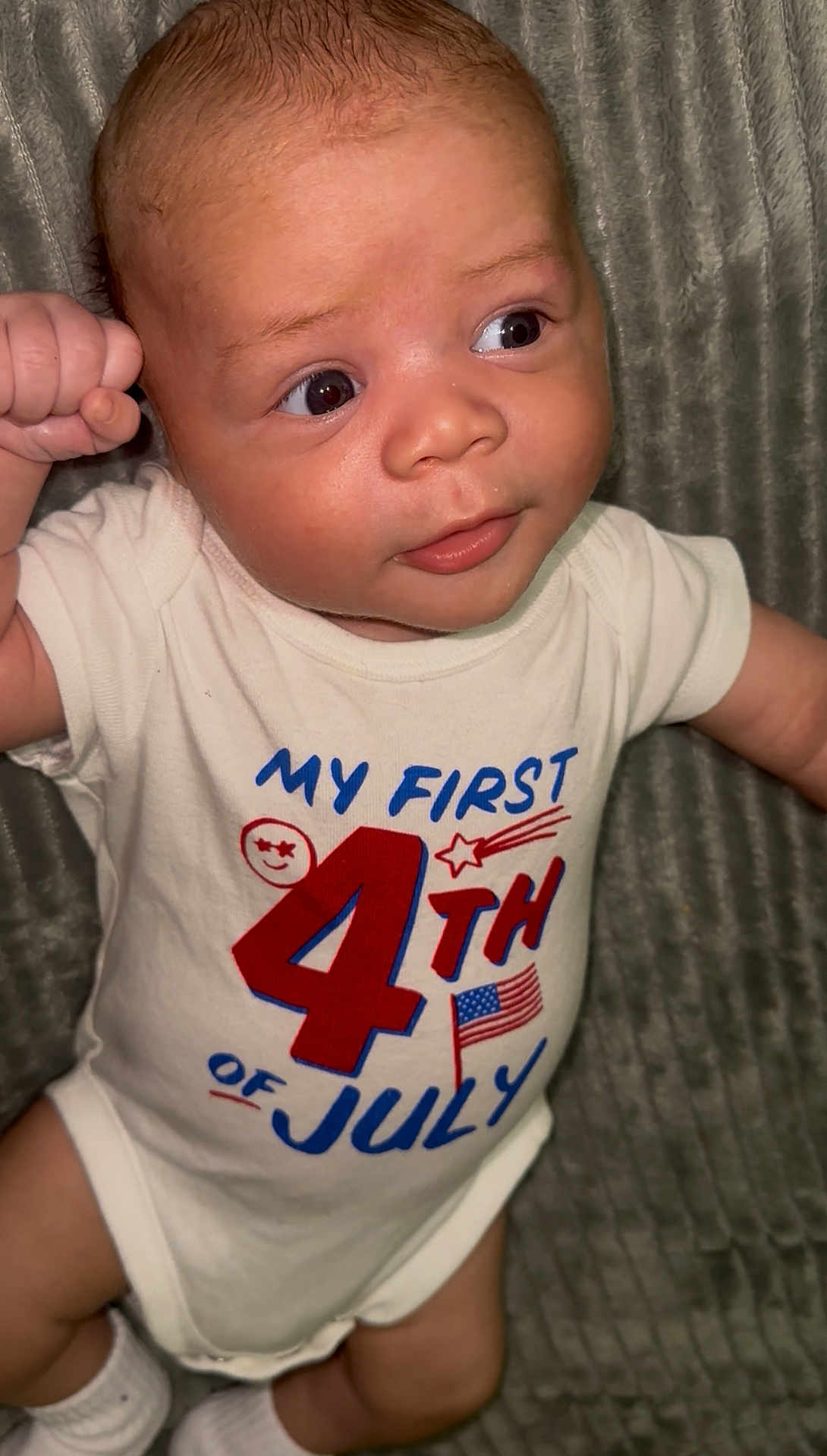 Adonnis is registered to the contest to win money with this photo: baby, infant, onesie, clothing, smile, face, eyes, hand, footwear, sock, blanket, celebration, holiday, american_flag, text, pose, cute, portrait, child, indoors