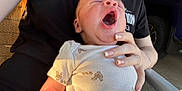 Adonnis joined the competition — help win amazing prizes! baby, yawning, infant, person, hand, clothing, onesie, footprint_pattern, skin, outdoor, sunlight, black_shirt, fingernails, car_tire, arm, closeup, holding, casual, relaxing, seat
