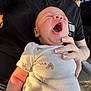 baby, yawning, infant, person, hand, clothing, onesie, footprint_pattern, skin, outdoor, sunlight, black_shirt, fingernails, car_tire, arm, closeup, holding, casual, relaxing, seat
