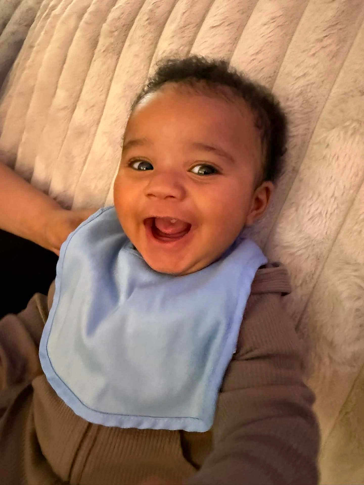 Karsyn joined the competition — help win amazing prizes! baby, smiling, bib, brown_clothing, lying_down, happy, infant, face, cute, child, plush_blanket, closeup, portrait, indoors, soft_texture, joyful, young_child, skin, head, expression