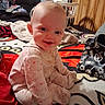 baby, infant, pajamas, smile, child, indoor, blanket, pattern, furniture, laundry_basket, clothing, person, home, wood_paneling, bag, toy, floor, happy, seated, cozy