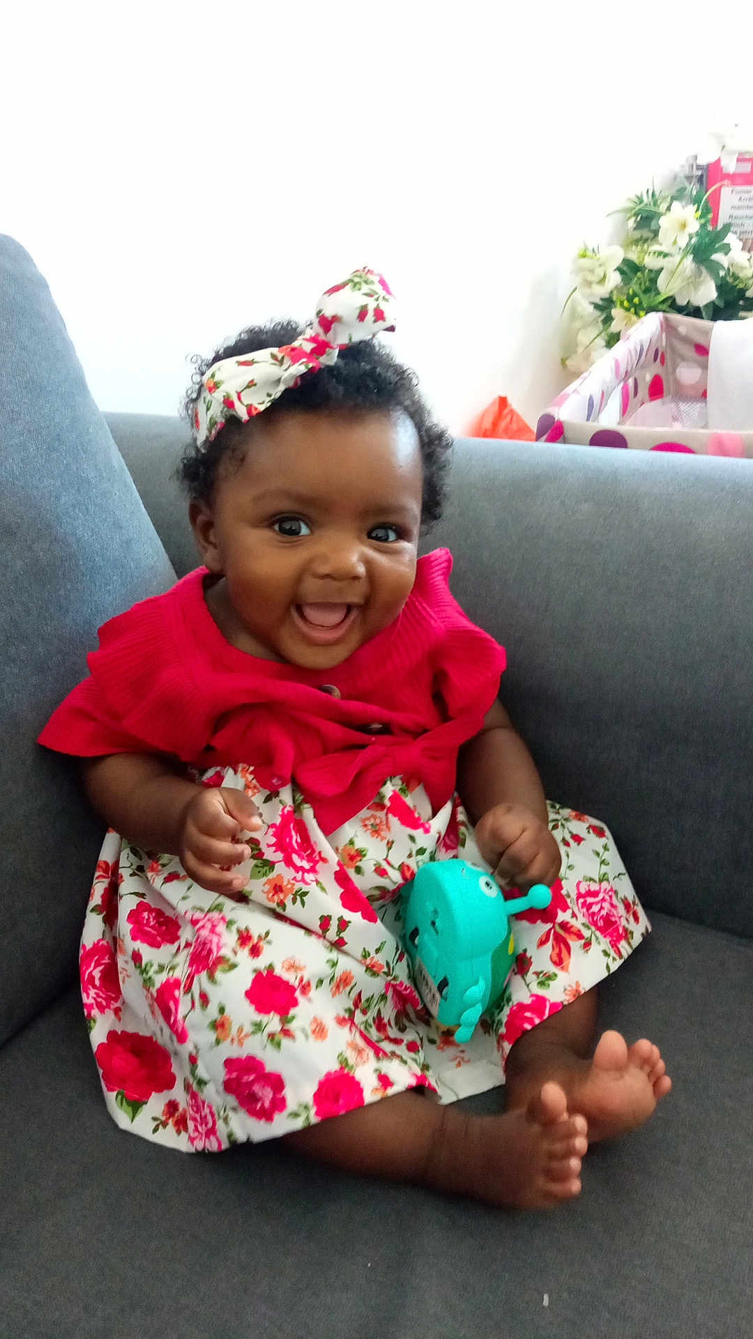 Soriah participe au concours pour gagner de l'argent avec cette photo : baby, child, smiling, dress, headband, toy, sitting, couch, indoor, happy, curly_hair, barefoot, floral_pattern, person, infant, cute, colorful, playful, young, portrait