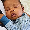 baby, sleeping, infant, child, blue_clothing, animal_print, couch, cushion, peaceful, resting, indoor, closeup, portrait, young_child, relaxing, soft_texture, head, face, hand, cozy