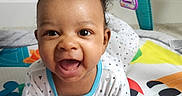 Azariah is registered to the contest to win money with this photo: baby, infant, smile, playmat, toy, colorful, child, happy, face, clothing, indoor, cute, hands, lying_down, curly_hair, baby_gym, floor, pattern, expression, toddler