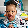 baby, infant, smile, playmat, toy, colorful, child, happy, face, clothing, indoor, cute, hands, lying_down, curly_hair, baby_gym, floor, pattern, expression, toddler