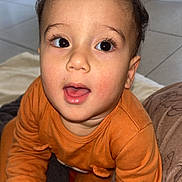 Nahyl a rejoint le concours — aidez-le/la à gagner de superbes lots ! baby, blanket, child, curly_hair, cute, expression, face, floor, hand, happy, home, indoor, long_sleeve, orange_clothing, person, portrait, sitting, skin, toddler, young