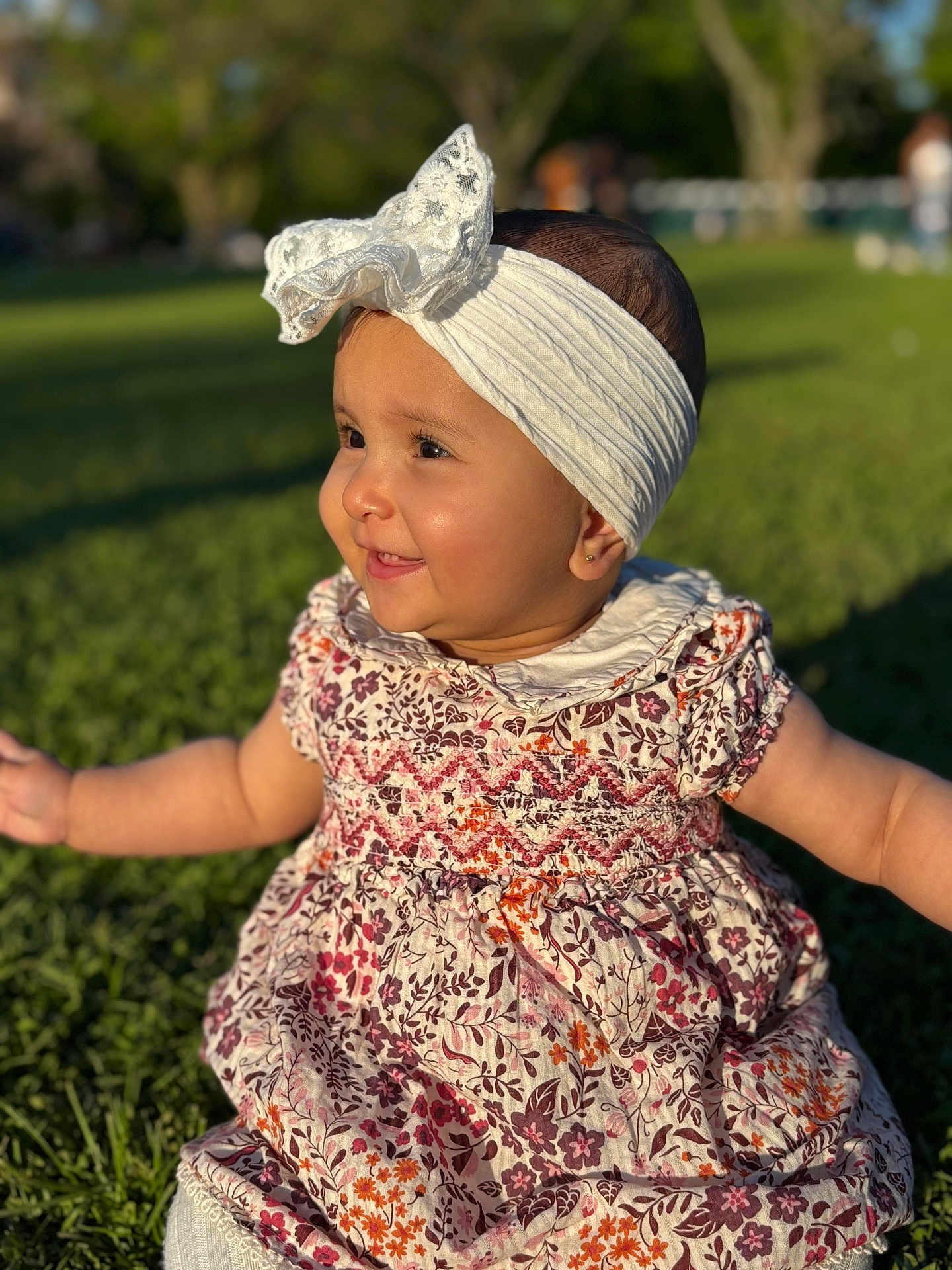 Rima joined the competition — help win amazing prizes! baby, child, girl, smiling, headband, bow, floral_dress, grass, outdoor, sunlight, park, happy, cute, portrait, nature, sitting, person, head, face, young_child