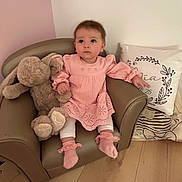 Mïa participe au concours pour gagner de l'argent avec cette photo : armchair, baby, child, cute, decor, floor, furniture, indoor, infant, nursery, person, pillow, pink_dress, plush_toy, sitting, sock, soft_toy, wall, white_legwear, wooden_floor