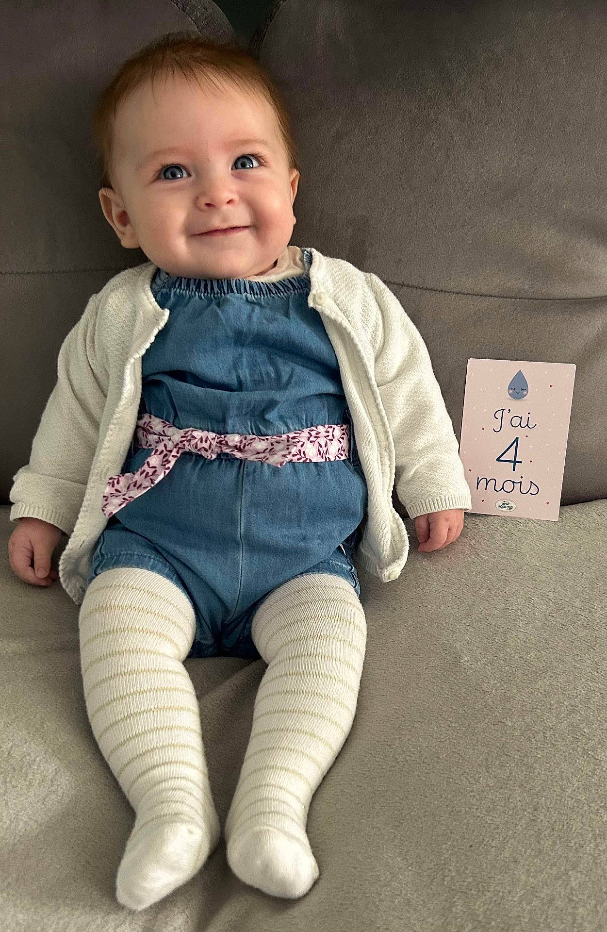 baby, blue_eyes, cardigan, child, clothing, comfortable, couch, cute, fabric, four_months, happy, indoor, infant, milestone_card, person, portrait, sitting, smiling, striped_tights, text