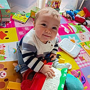 Sacha participe au concours pour gagner de l'argent avec cette photo : baby, child, toy, play_mat, colorful, indoor, smiling, sitting, striped_sweater, face, hand, plastic_toy, soft_toy, floor, learning_toys, cute, young_child, early_childhood, happy, casual_clothing