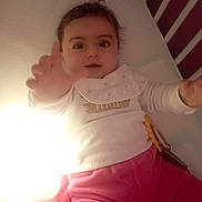 Ambre a rejoint le concours — aidez-le/la à gagner de superbes lots ! baby, infant, crib, reaching_hand, pink_pants, white_shirt, bib, light, wooden_background, indoor, cute, child, person, smiling, face, eyes, hand, sleeping_area, soft_toys, cozy