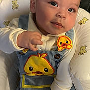 Dylan is registered to the contest to win money with this photo: baby, infant, child, face, eyes, clothing, overalls, duck_patch, hand, baby_seat, teddy_bear_pattern, cute, portrait, skin, sitting, soft_lighting, indoor, cozy, comfortable, expression