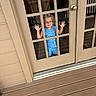 Merrick is registered to the contest to win money with this photo: blue_clothing, casual, child, curious, door_knob, face, glass_door, hands, happy, home, indoor, natural_light, outside_view, person, reflection, shark_pattern, smile, toddler, window_panes, wooden_porch