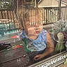 background, child, clothing, curious, daylight, deck, face, fence, home, house, outdoor, person, play, portrait, railing, reflection, toddler, toy, tractor, window_screen