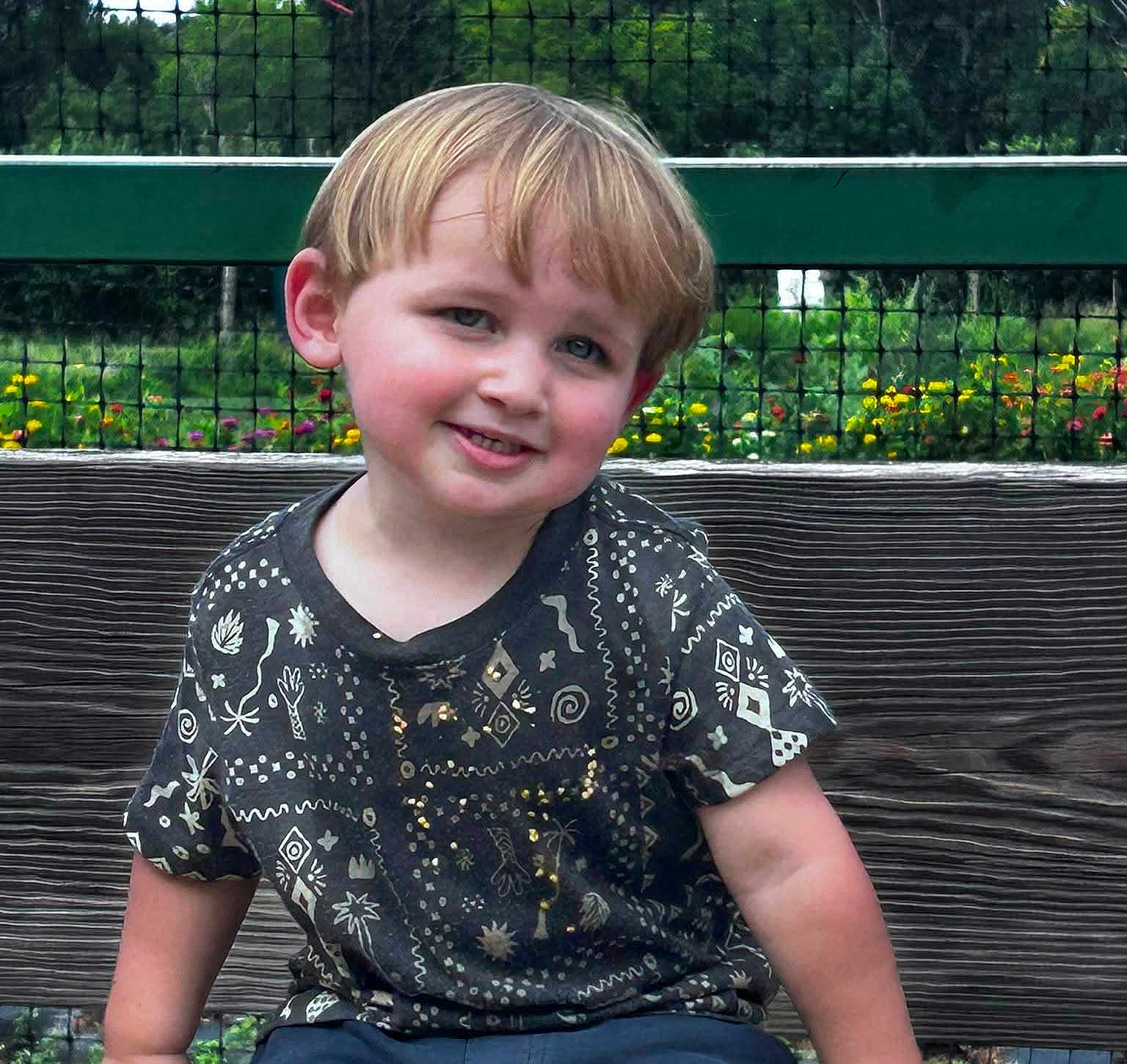 Levi joined the competition — help win amazing prizes! child, boy, smiling, sitting, bench, outdoor, garden, flowers, greenery, fence, casual_clothing, short_hair, daylight, portrait, happy, nature, wood, playful, park, cute