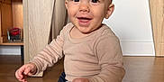 Hélio a rejoint le concours — aidez-le/la à gagner de superbes lots ! baby, child, smiling, sitting, floor, wooden_floor, long_sleeve_shirt, pants, indoors, home, furniture, shelf, toy, happy, face, person, cute, infant, young_child, natural_light
