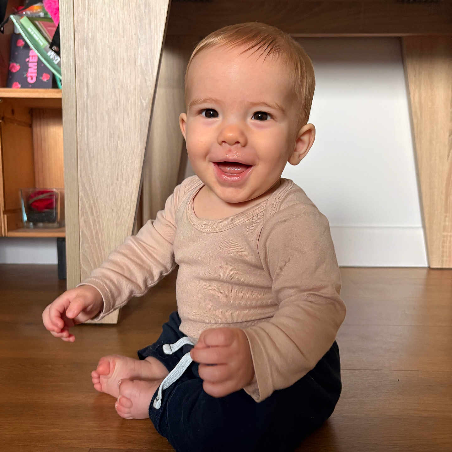Hélio a rejoint le concours — aidez-le/la à gagner de superbes lots ! baby, child, cute, face, floor, furniture, happy, home, indoors, infant, long_sleeve_shirt, natural_light, pants, person, shelf, sitting, smiling, toy, wooden_floor, young_child