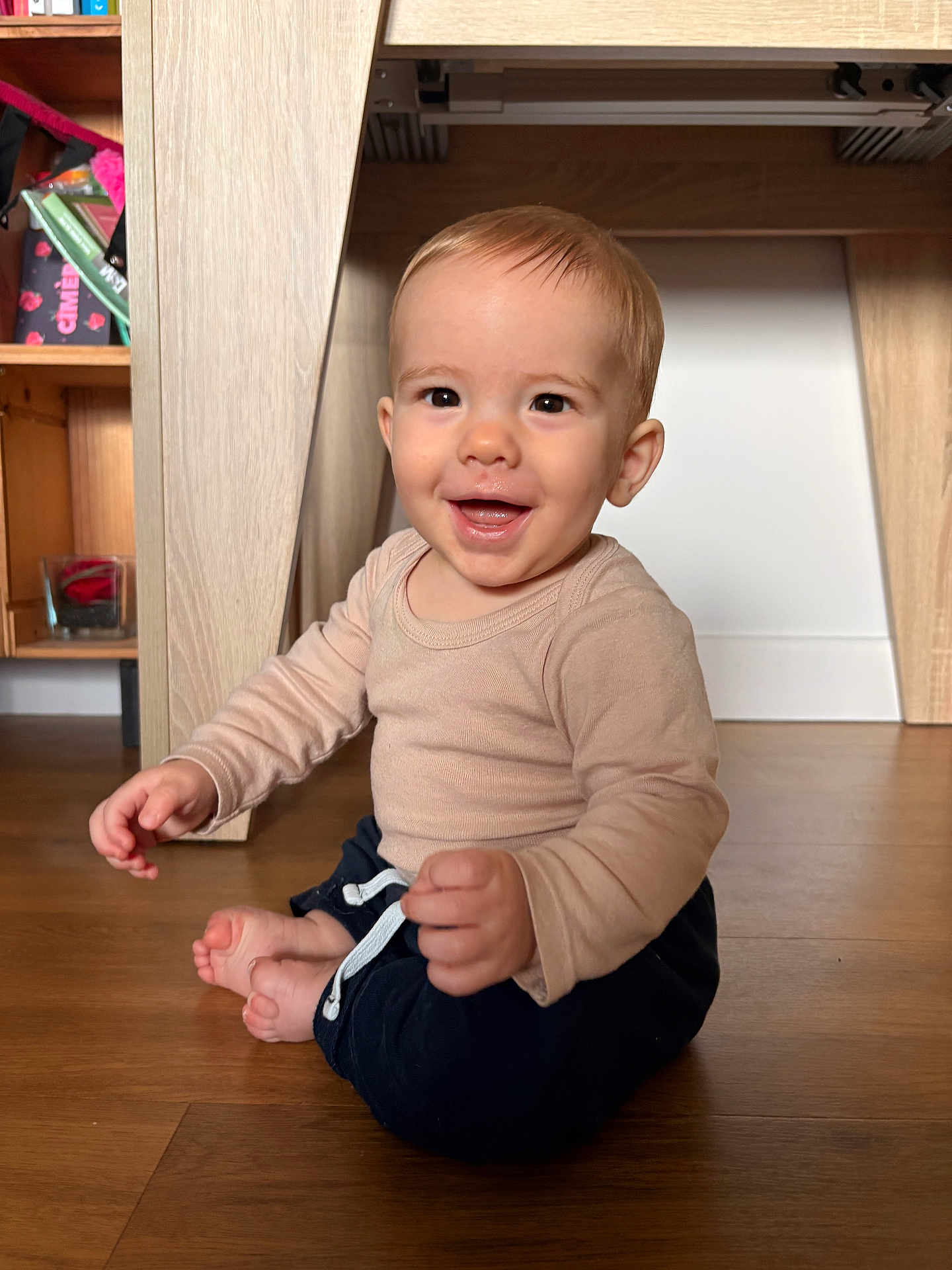 Hélio a rejoint le concours — aidez-le/la à gagner de superbes lots ! baby, child, smiling, sitting, floor, wooden_floor, long_sleeve_shirt, pants, indoors, home, furniture, shelf, toy, happy, face, person, cute, infant, young_child, natural_light