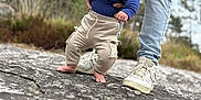 Kalvynn a rejoint le concours — aidez-le/la à gagner de superbes lots ! baby, child, person, tattoo, jeans, shirt, sneakers, rock, outdoor, nature, grass, cloudy_sky, walking, supporting_hands, determined, serious_face, barefoot, pants, blue_shirt, casual