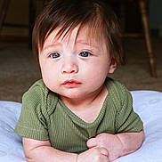 Parker is registered to the contest to win money with this photo: baby, blue_eyes, brown_hair, child, closeup, cushion, cute, expression, face, green_shirt, hands, indoor, infant, lying_down, person, portrait, skin, soft_light, toddler, young