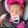 baby, pacifier, car_seat, pink_bow, blanket, child, infant, headband, seatbelt, clothing, cute, face, portrait, sitting, indoors, young_child, safety, resting, expression, toddler