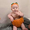 baby, pumpkin, hat, orange, smiling, cute, child, sitting, indoors, cheerful, soft, blanket, skin, headwear, one_person, infant, holiday, autumn, festive, playful