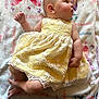 baby, child, infant, yellow_dress, floral_dress, blanket, butterfly_pattern, flower_pattern, laying_down, cute, soft_skin, small_hands, small_feet, curious_look, indoor, portrait, close_up, sleepwear, fabric, cozy