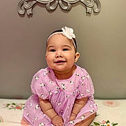 Raelynn is registered to the contest to win money with this photo: baby, infant, child, smiling, headband, flower, purple_dress, floral_pattern, sitting, portrait, cute, happy, chubby_cheeks, toes, hands, indoor, headboard, bedding, soft_lighting, closeup