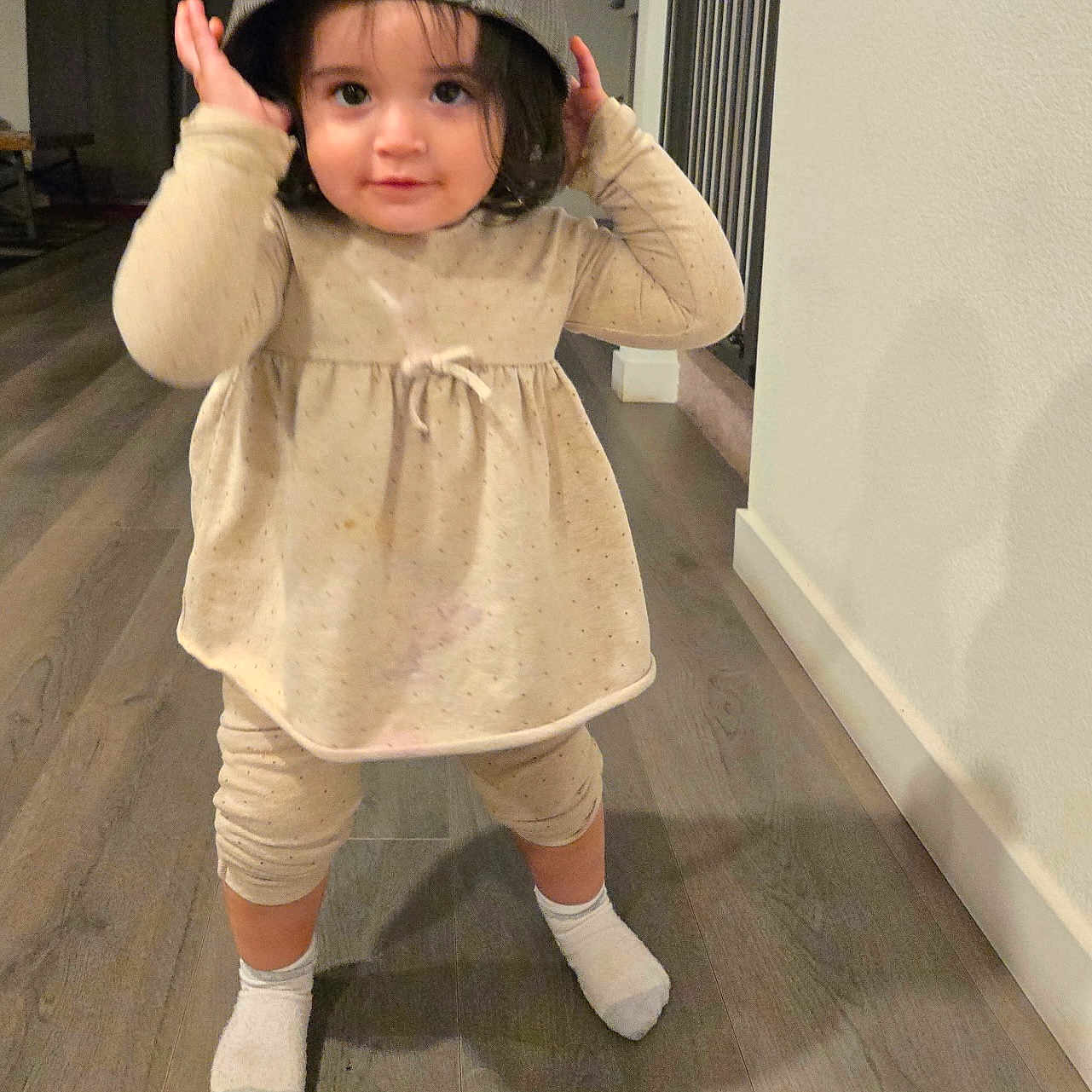 Melissa Arellano joined the competition — help win amazing prizes! baseball_cap, beige_clothing, casual, child, cute, floor, hair, home, indoor, lighting, long_hair, person, playful, smiling, socks, standing, toddler, wall, wood_floor, young_child