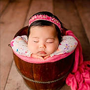 Rulena is registered to the contest to win money with this photo: baby, sleeping, headband, wooden_bucket, pink_blanket, floral_pattern, infant, close_up, portrait, cozy, peaceful, hands_under_chin, indoors, flooring, cute, newborn, soft_lighting, resting, child, adorable