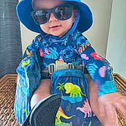 Bentlee joined the competition — help win amazing prizes! toddler, child, baby, blue_hat, sunglasses, booster_seat, dinosaur_pattern, colorful_clothing, indoor, woven_surface, smiling, reaching_hand, seatbelt, playful, cute, portrait, person, hat, footwear, bright_colors